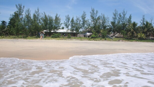 A beach with a sandy shore and waves. There are trees and a few buildings in the background. - Chez Paul Ambodiatafana (Ambodiatafana)