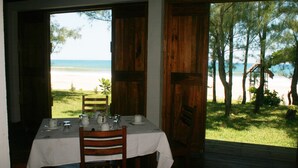 A dining table set with white tablecloth, plates, and glasses, overlooking a beach with trees and a wooden deck. - Chez Paul Ambodiatafana (Ambodiatafana)