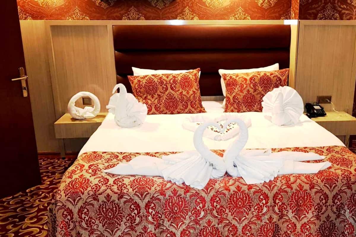 A hotel room with a large bed, two pillows, a bedside table with a phone, and a wall-mounted lamp.