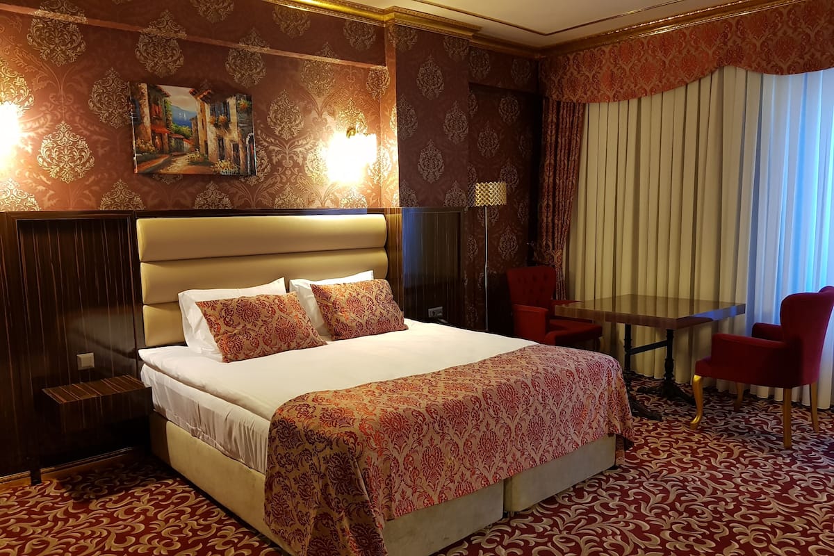 A hotel room with a large bed, a desk, two chairs, and a painting on the wall.