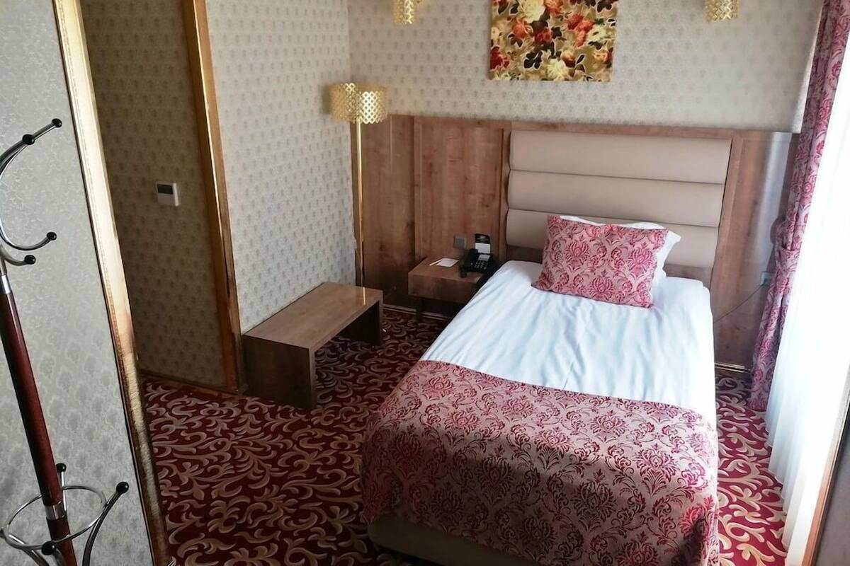 A hotel room with a bed, bedside table, lamp, and a floral artwork on the wall.