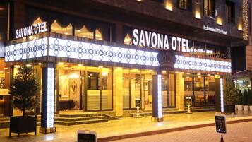 Exterior de l'Hotel Savona amb cartelleria il·luminada, una entrada imponent i una façana ben il·luminada.