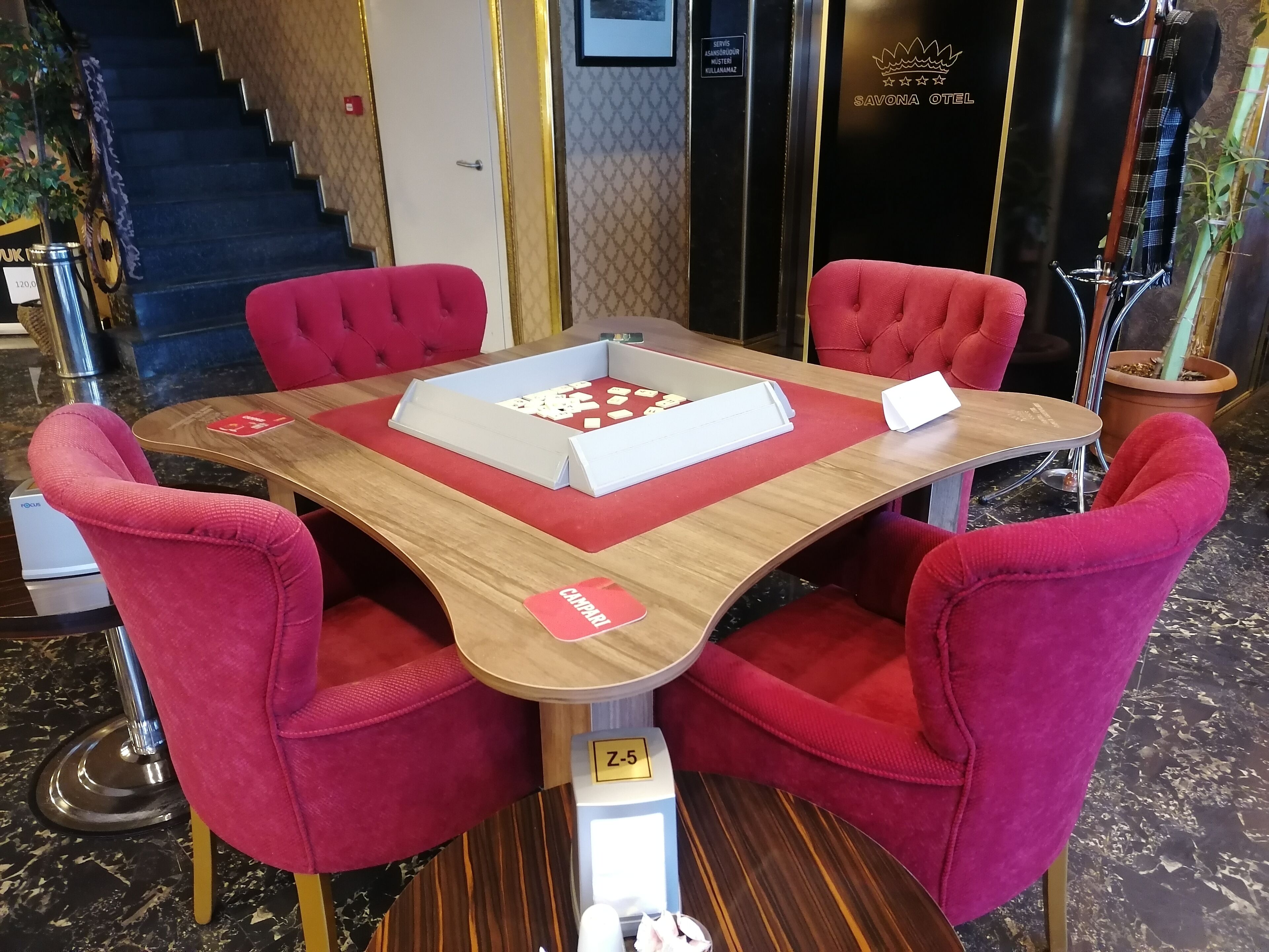A hotel lobby with a round table and four red upholstered chairs. A white tray with a card and a small object is on the table.