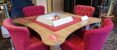 Un vestíbulo de hotel con una mesa redonda y cuatro sillas tapizadas rojas. Una bandeja blanca con una tarjeta y un objeto pequeño está sobre la mesa.