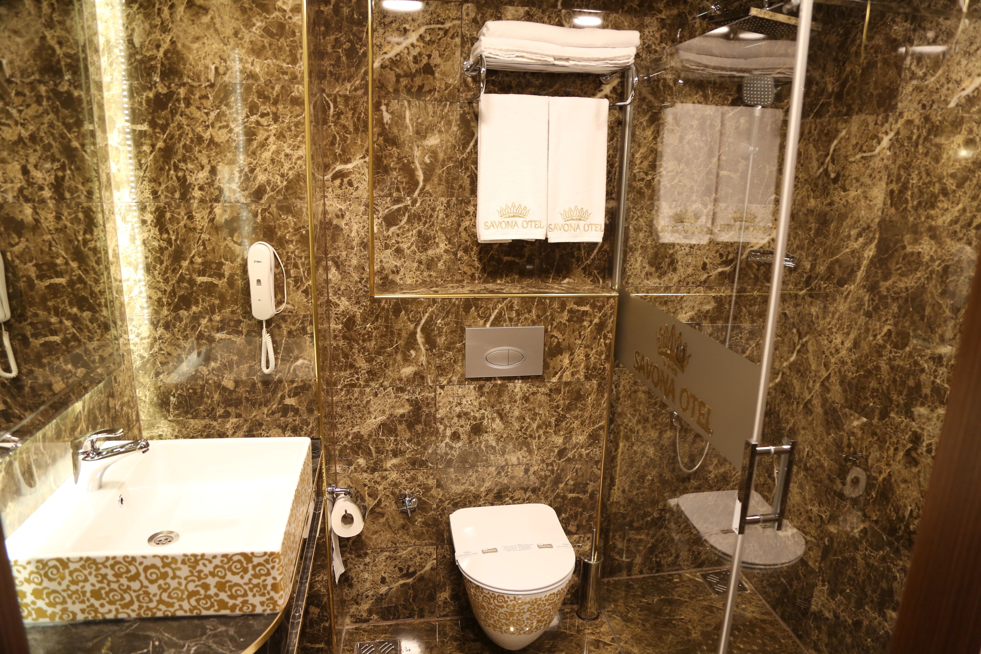 A bathroom with a marble wall, a sink, a toilet, and a glass shower enclosure.