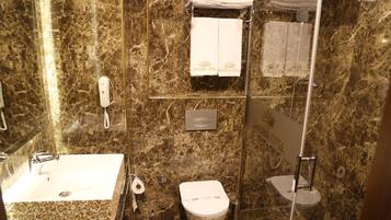 A bathroom with a marble wall, a sink, a toilet, and a glass shower enclosure.