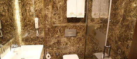 A bathroom with a marble wall, a sink, a toilet, and a glass shower enclosure.