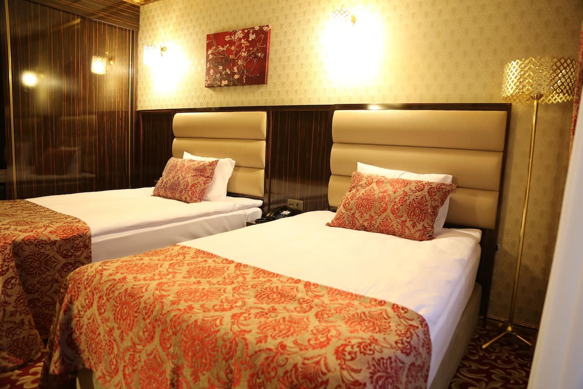 A hotel room with two beds, each with a patterned bedspread and pillows, a headboard, a wall-mounted light, and a floor lamp.