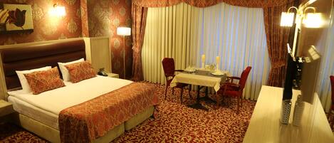 Habitación de hotel con una cama grande, una mesa de comedor con sillas, un espejo y una alfombra estampada.