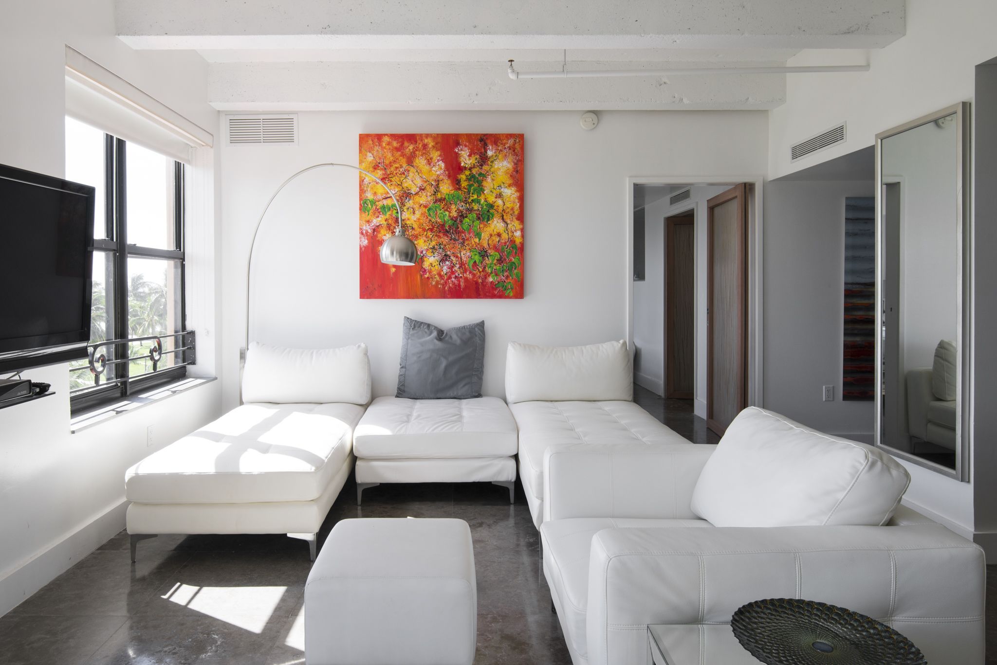 A modern living room with a white sofa set, a flat-screen TV, and a large abstract painting.