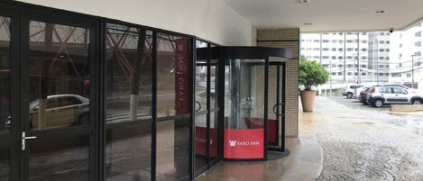 A hotel entrance with a revolving door, glass doors, and a tiled pavement.
