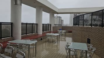 A rooftop patio with metal tables and chairs, a brick wall, and a view of tall buildings.