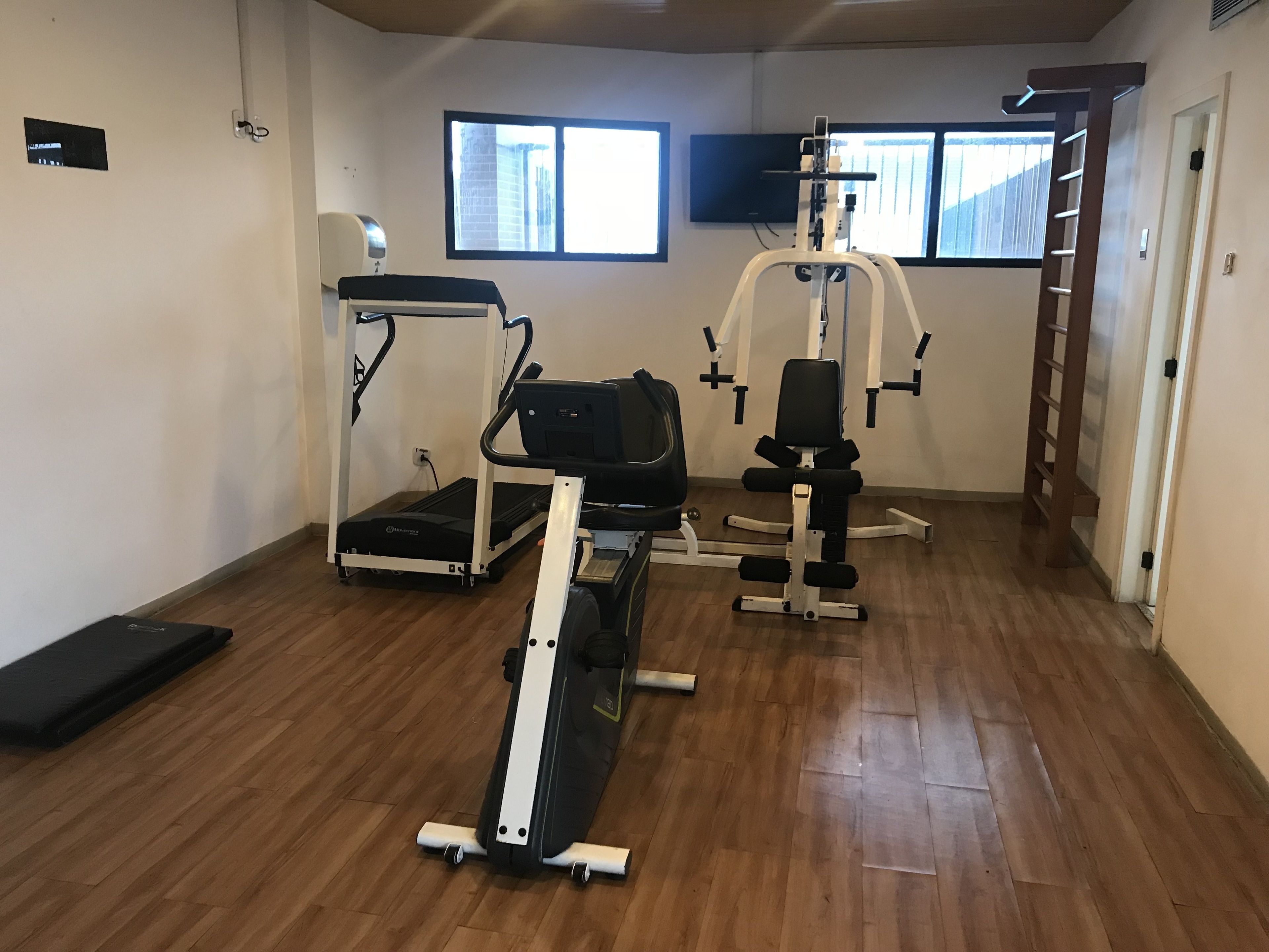 A gym with cardio machines, weightlifting equipment, and a wooden floor.