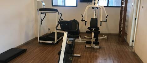 Un gimnasio con máquinas de cardio, equipo de levantamiento de pesas y piso de madera.
