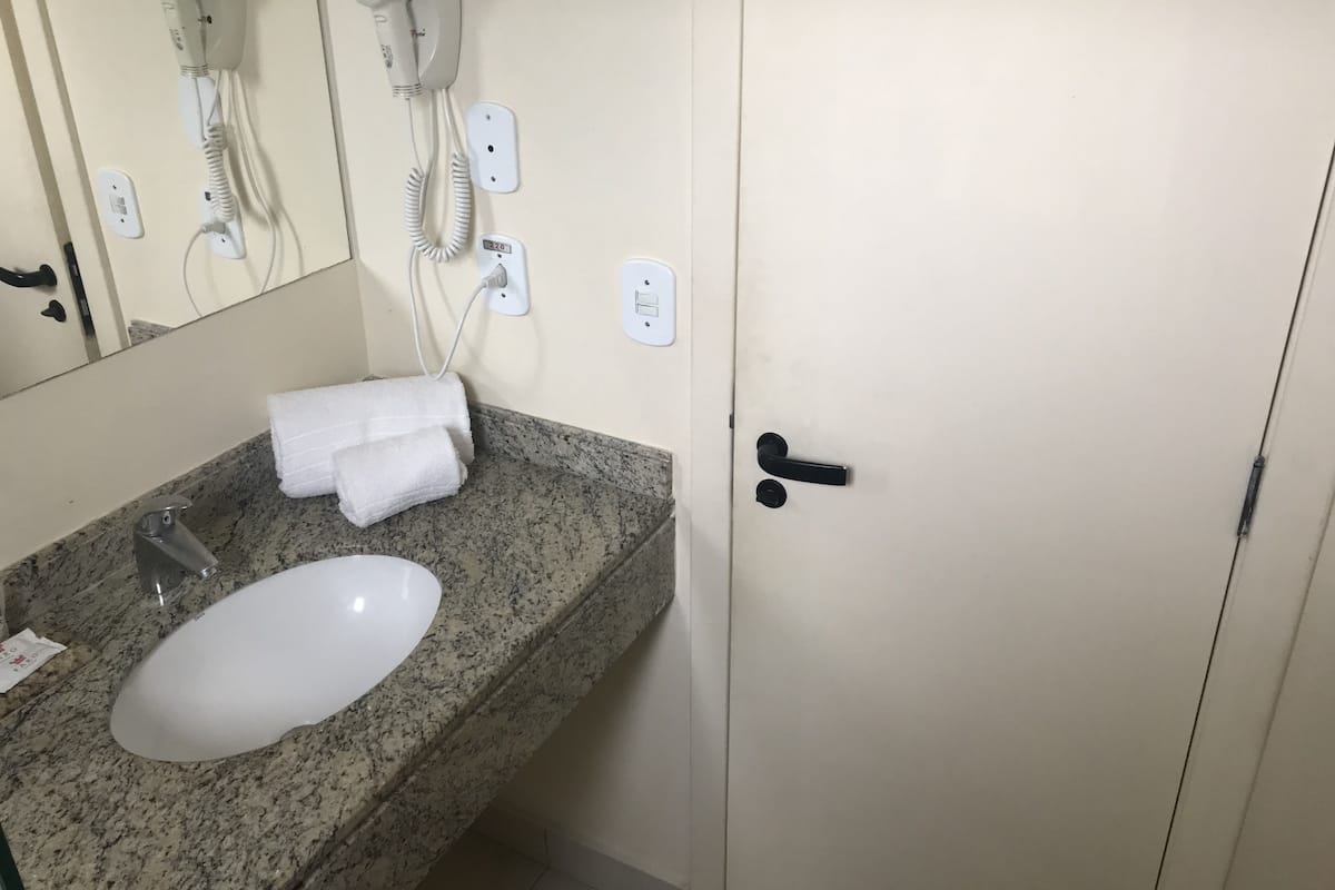 Un baño con encimera de granito, un lavamanos blanco, una toalla, un secador de pelo y una puerta.