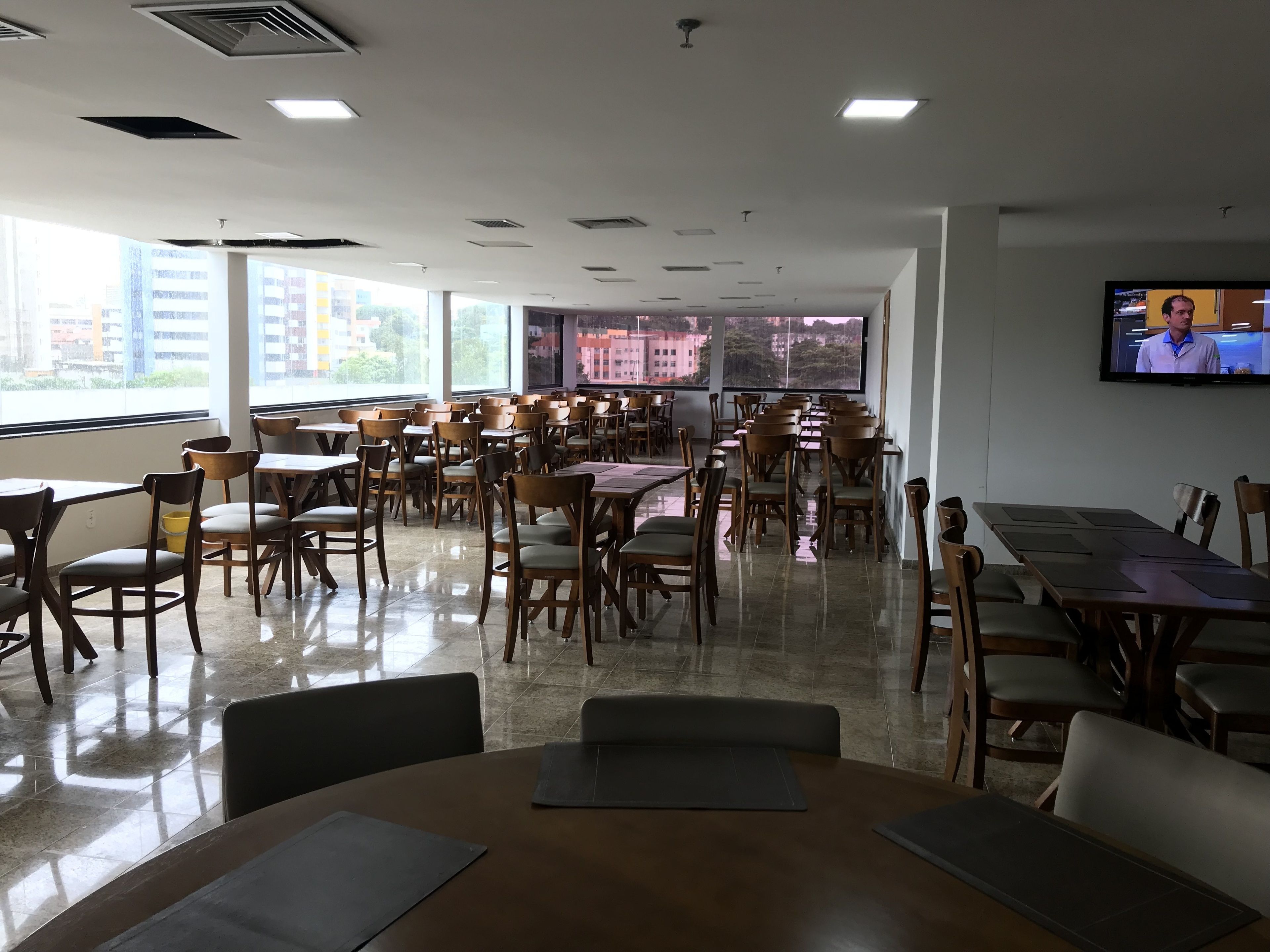 A conference room with multiple tables and chairs, large windows with a city view, and a television on the wall.