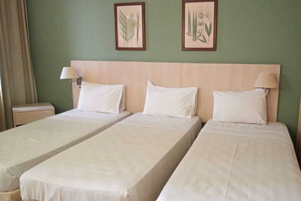 Habitación de hotel con dos camas individuales, cabecero de madera y dos lámparas de pared.