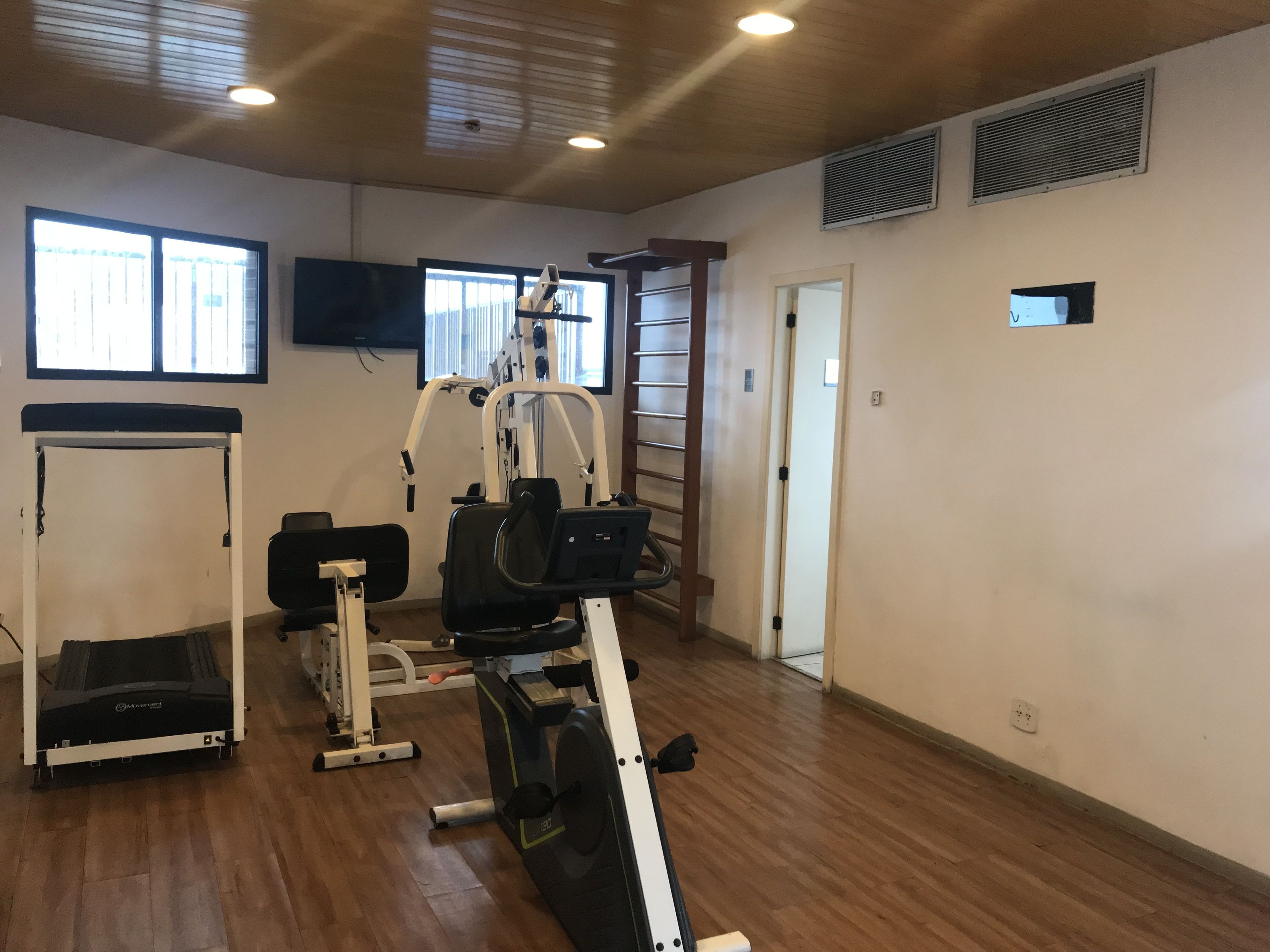 A gym with cardio machines, a weight bench, and a wall-mounted TV.