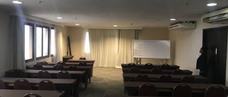 Ein Konferenzraum mit Tischen, Stühlen, einer Whiteboard und einer Projektionsleinwand.