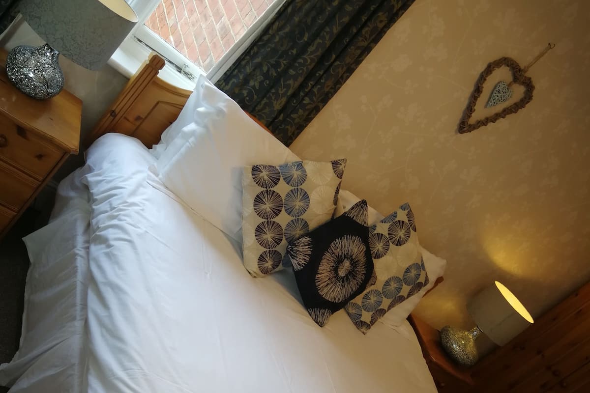 A neatly made bed with white linens, a decorative pillow, and a rolled towel.