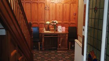 A wooden-paneled room with a desk, chairs, a chandelier, and a patterned carpet.