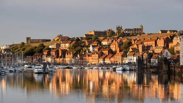 A harbor with boats and buildings reflecting on the water. - The Grove (Whitby)