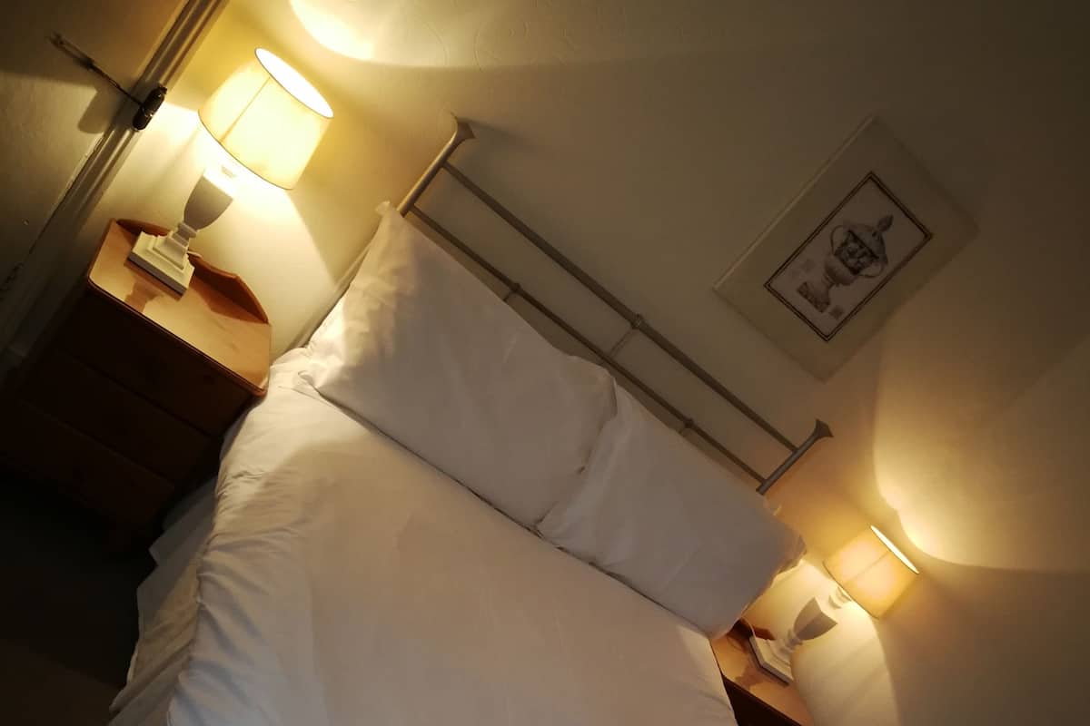 A neatly made bed with white linens and two rolled towels, a bedside lamp, and a framed picture on the wall.