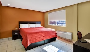A bedroom with a bed, a nightstand, a desk, and a window with a view.
