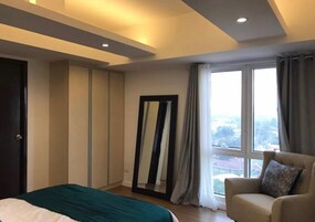 Una habitación de hotel moderna con una cama, una silla, un ventanal grande y un espejo.