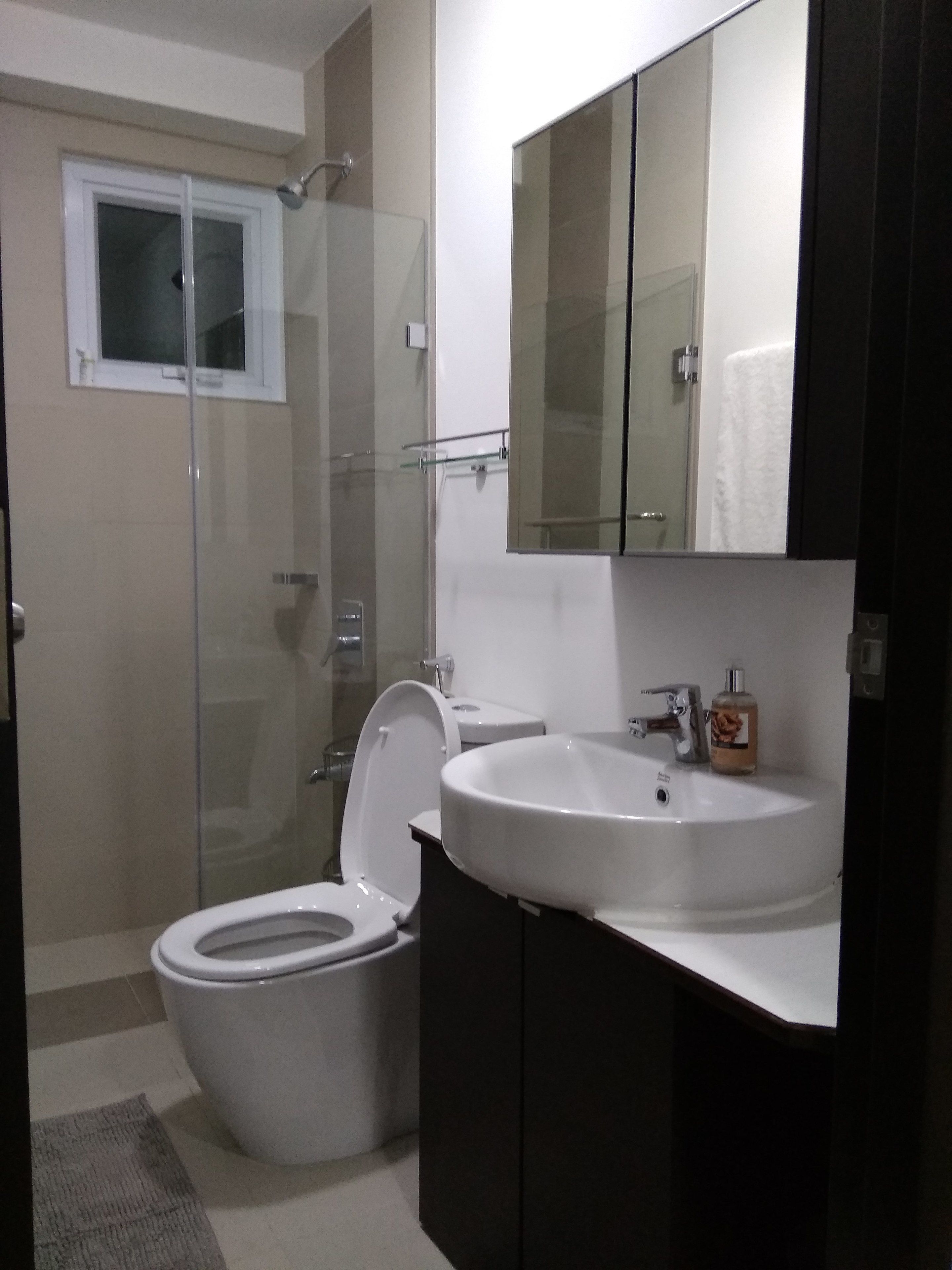 Ein modernes Badezimmer mit Duschkabine aus Glas, einer weißen Toilette und einem großen Waschbecken mit Spiegel darüber.