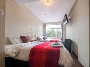 A hotel room with two beds, a TV mounted on the wall, a window with curtains, and a ceiling light. - Pikaflor B&B (Cusco)