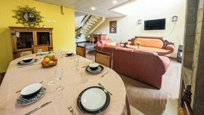 Uma área de refeições com uma mesa redonda posta para quatro pessoas, um sofá, uma escada e uma TV fixada na parede.