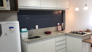 A modern kitchen with white cabinets, a black tiled backsplash, a built-in microwave, a gas stove, and pendant lighting. - Ondina Apart Hotel (Salvador)