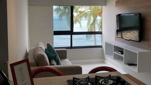 A modern kitchen with a gas stove, a dining area with a red chair, and a large window with a view of the sea. - Ondina Apart Hotel (Salvador)