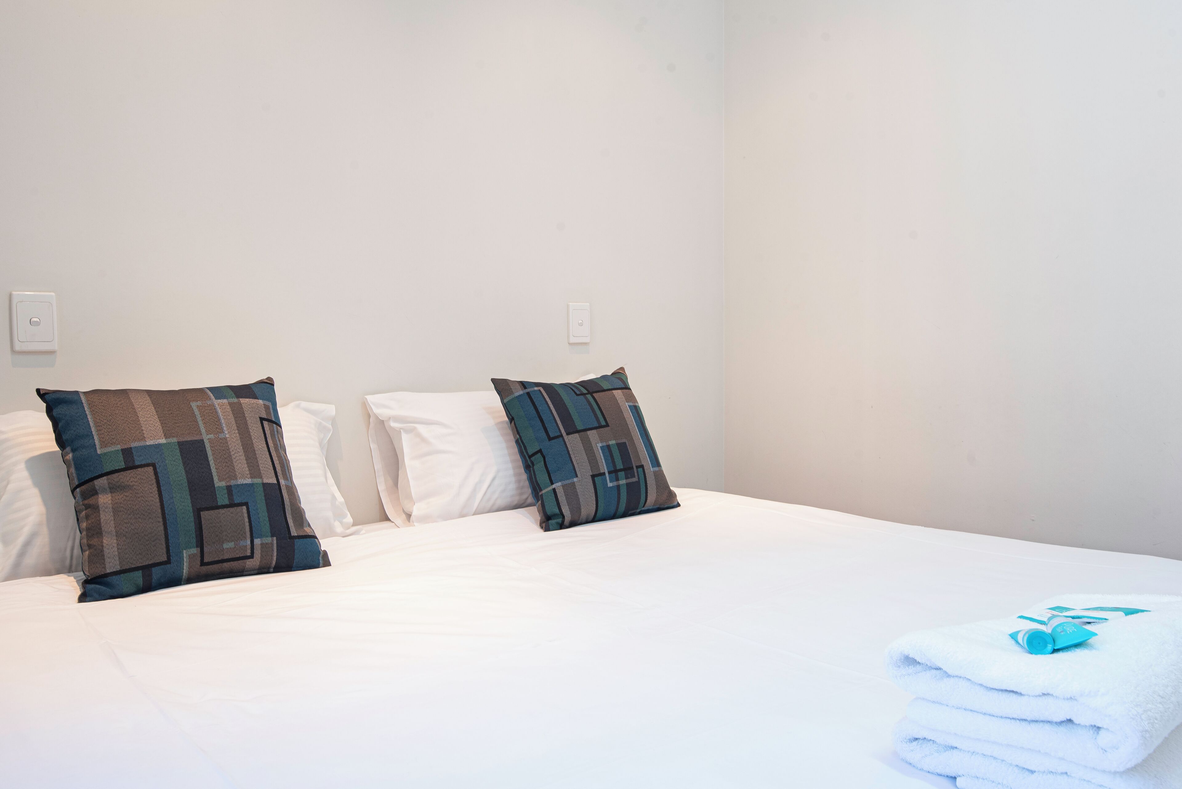 A neatly made bed with two patterned pillows and a folded white towel on a white bedspread.