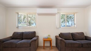 Una habitación con dos sofás marrones, una mesita de madera y un aire acondicionado ubicado entre dos ventanas.