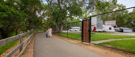 A paved walkway with a wooden fence on one side and a chain-link fence on the other, leading to a gated area with a sign prohibiting public toilets.