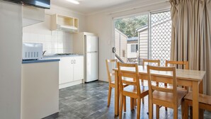 Cocina compacta con armarios blancos, un refrigerador y un comedor con sillas de madera y una mesa.