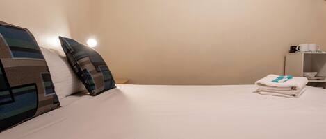 Una cama bien hecha con almohadillas a rayas, un cuadro en la pared y una pila de toallas dobladas en la mesita de noche.