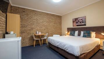 Habitación de hotel con pared de ladrillo, cama con ropa blanca, escritorio y dos sillas, y un cuadro en la pared.