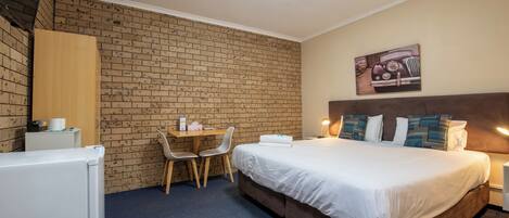 A hotel room with a brick-patterned wall, a bed with white bedding, a desk with two chairs, and a painting on the wall.