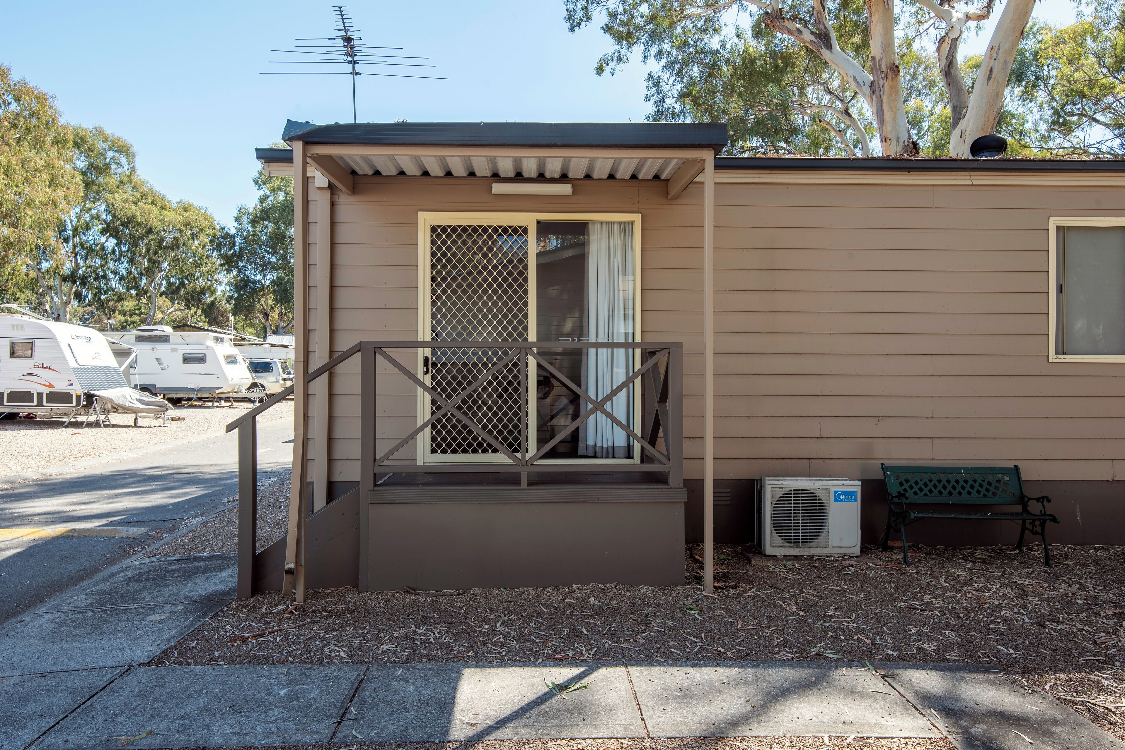 A small building with a porch, a bench, and an air conditioning unit.