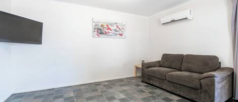 A room with a gray tiled floor, a brown sofa, a flat-screen TV mounted on the wall, and a ceiling light.