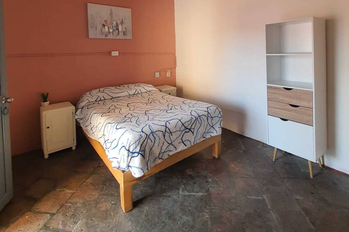 Een slaapkamer met een bed, een plafondventilator, een nachtkastje, een wandplank en een deur.