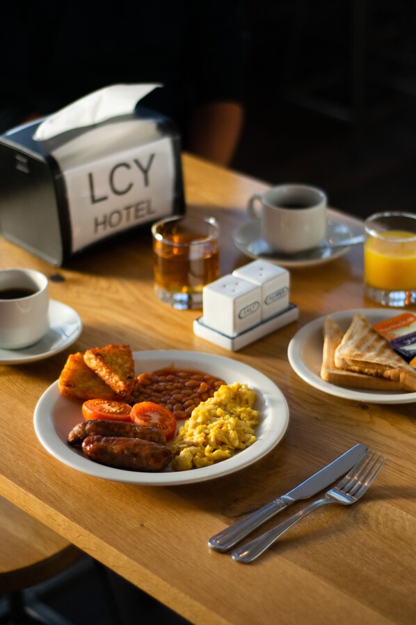 Une table de petit-déjeuner avec des assiettes de nourriture, une tasse de café, un verre de jus d’orange et une pancarte indiquant le numéro de la chambre d’hôtel.