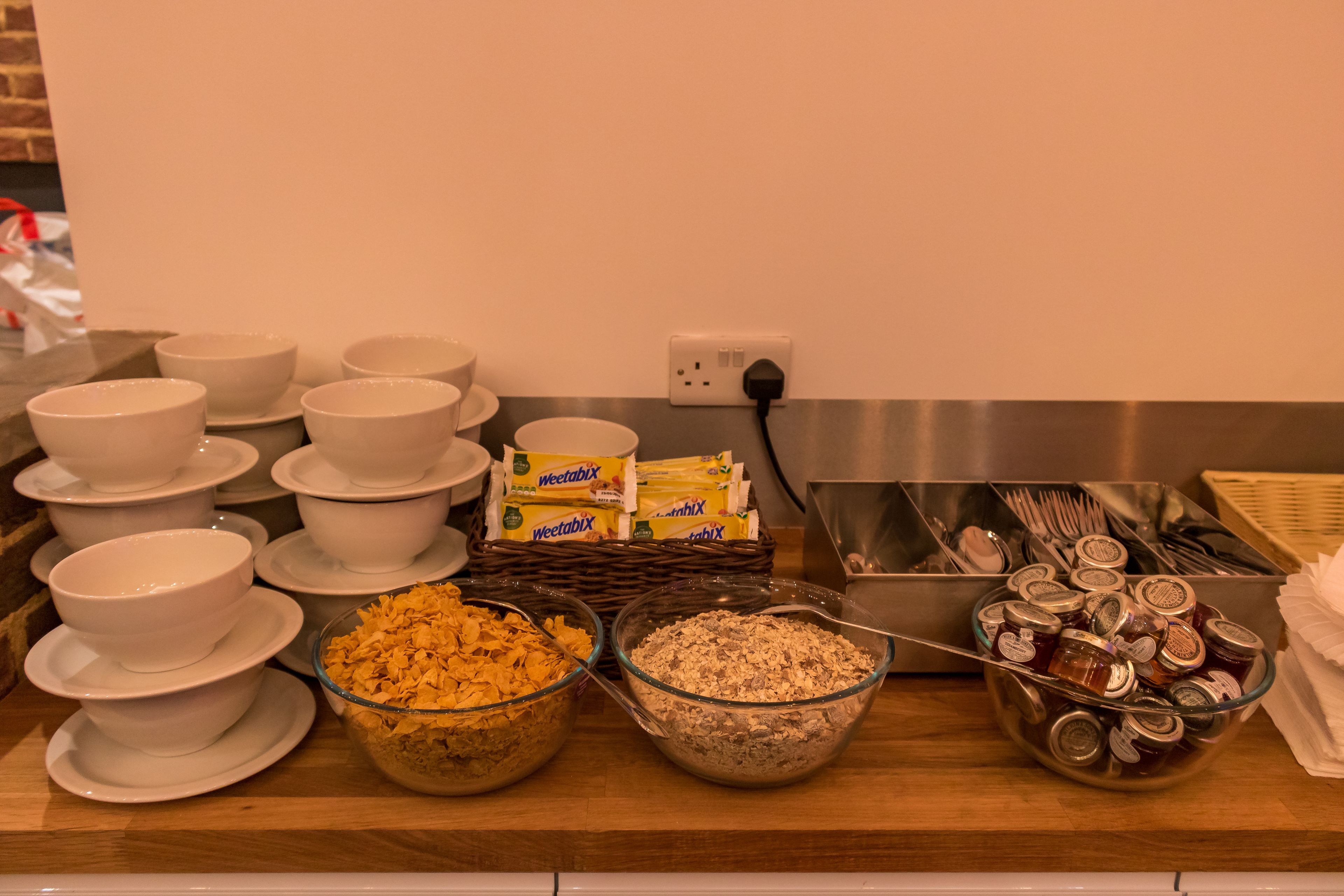 A buffet setup with bowls of cereal, a container of Weetabix, and utensils.