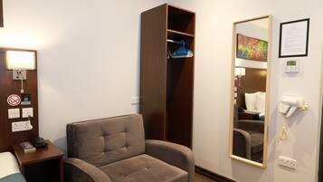 A hotel room with a single bed, a sofa, a wardrobe, a mirror, a hairdryer, and a wall-mounted phone.