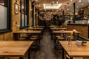 Un restaurant avec des tables et des chaises en bois, un mur en briques et des lampes suspendues.