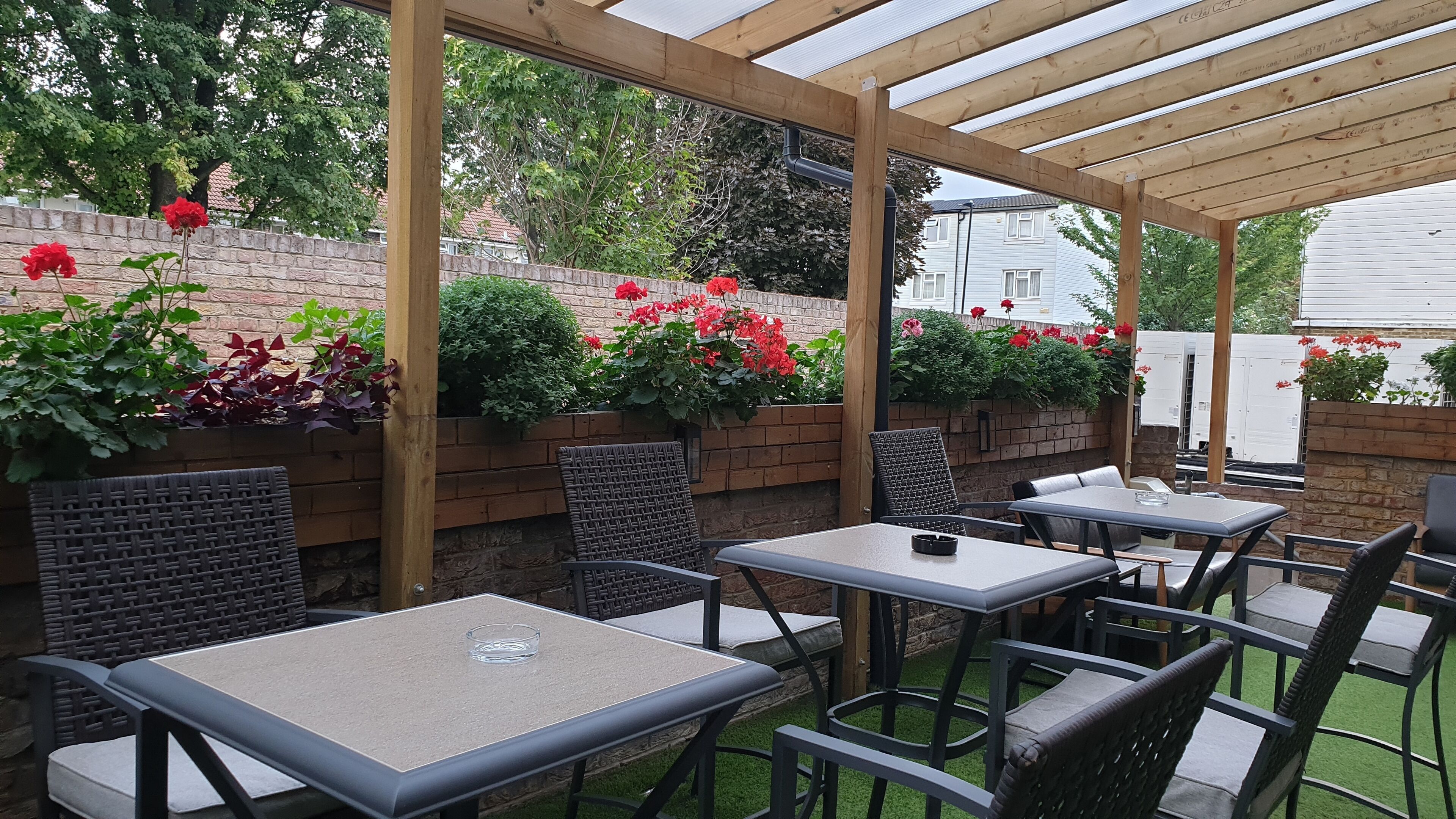 Eine Terrassengaststätte mit Tischen und Stühlen, umgeben von Ziegelmauern und Blumentöpfen.