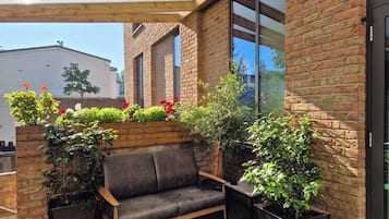 Un banco de madera con asiento y respaldo acolchados, rodeado de macetas con plantas y flores.